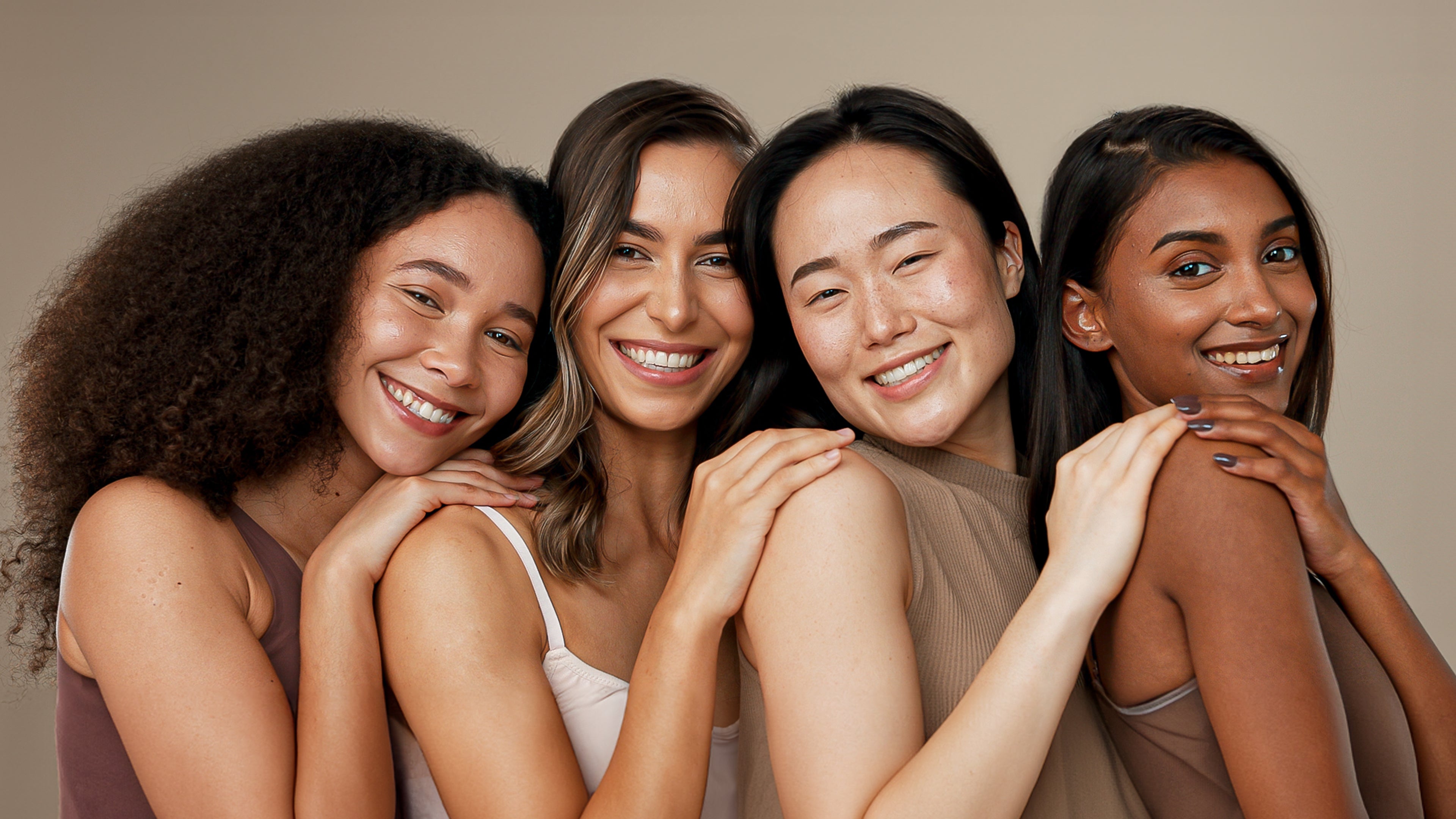 Four women with their hands on each other's shoulders, looking directly ahead and smiling brightly